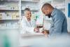 Medicine, shopping or pharmacist with customer writing personal or medical information in pharmacy. Consulting, pills or happy senior doctor helping or speaking to black man or sick African customer